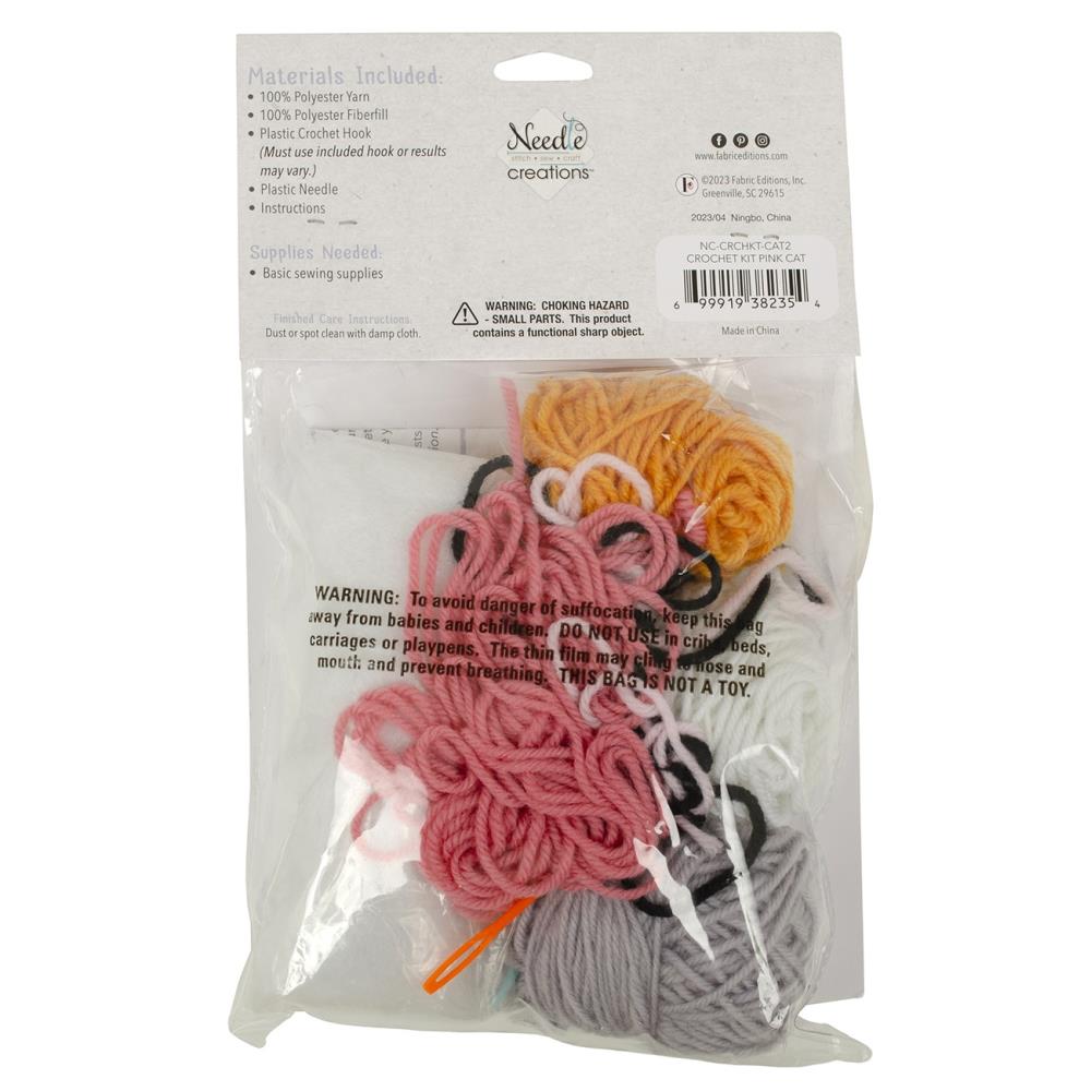 A flat lay of the Needle Creations kit: bundles of soft yarn, a bag of polyester stuffing, a crochet hook, and the clear instructional manual