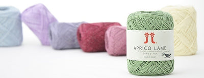 A compact ball of Japanese Aprico Lame cotton yarn, highlighting the vibrant color and the elegant, understated sparkle of the integrated metallic fibers