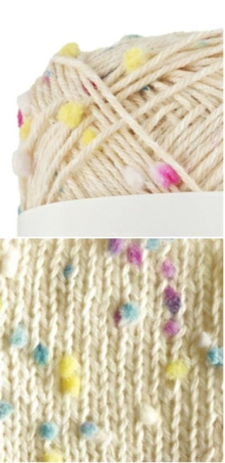 Close-up of yarn with colorful tiny pompom and a knitted fabric pattern.