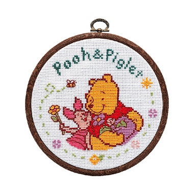 Cross-stitched design of a bear and girl with 'Pooh & Piglet' text in a wooden hoop.