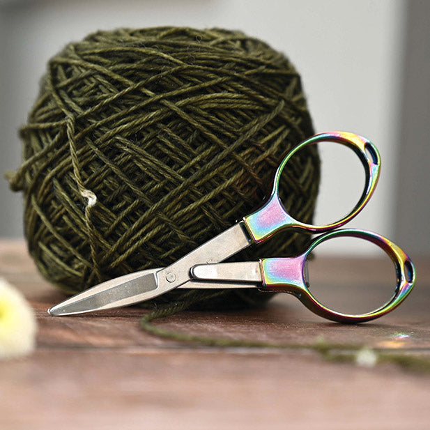 A close-up of the rainbow scissors with a ball of yarn behind showcasing the sharp, precision-pointed blades