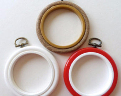 Three embroidery hoops in white, beige, and red colors, with plastic rims and metal screws for attachment.

A vibrant 3-inch circular plastic embroidery hoop with a matching adjustable tension screw, showing its smooth and colorful finish