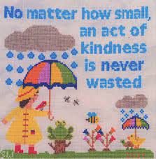 The "An Act of Kindness" cross stitch kit, showing the complete contents including premium embroidery floss, fabric, a needle, and the printed pattern sheet.