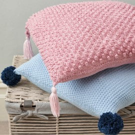 The book contains twelve exclusive English-language patterns for both knitting and crochet, featuring a range of newborn clothing, soft toys, nursery mobiles, and bedding accessories in a soft, modern aesthetic.