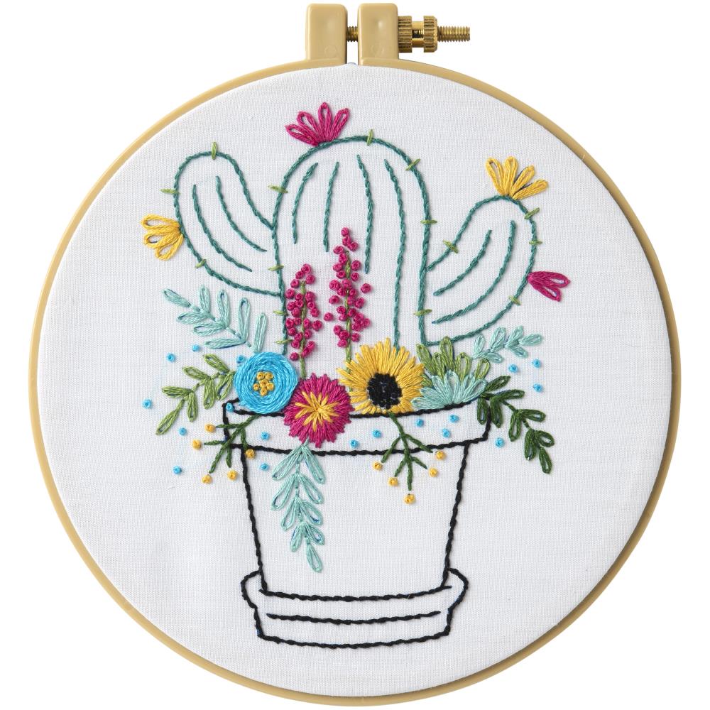 A beginner-friendly stamped embroidery kit from Bucilla titled 'Cactus Bloom.' The design features a colorful flowering cactus with vibrant pink blooms and green textures. The kit includes a pre-printed cotton-poly broadcloth, an array of cotton embroidery floss, a 6-inch plastic hoop, and a needle. The finished design is a 6-inch round circle
