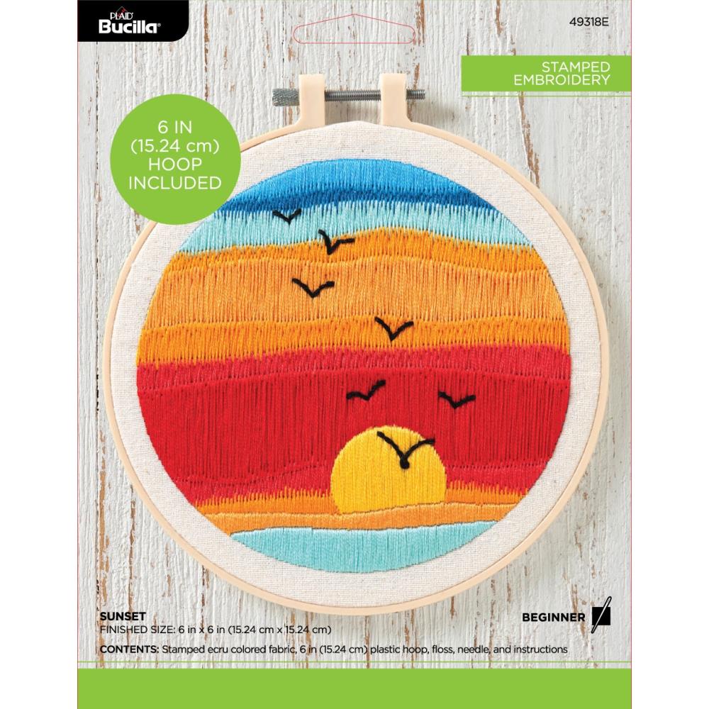 A beginner-friendly Bucilla stamped embroidery kit featuring a scenic sunset design. The kit includes a 6-inch round plastic hoop, a white broadcloth fabric pre-stamped with the sunset pattern, vibrant cotton embroidery floss in warm oranges and pinks, a needle, and easy-to-follow instructions