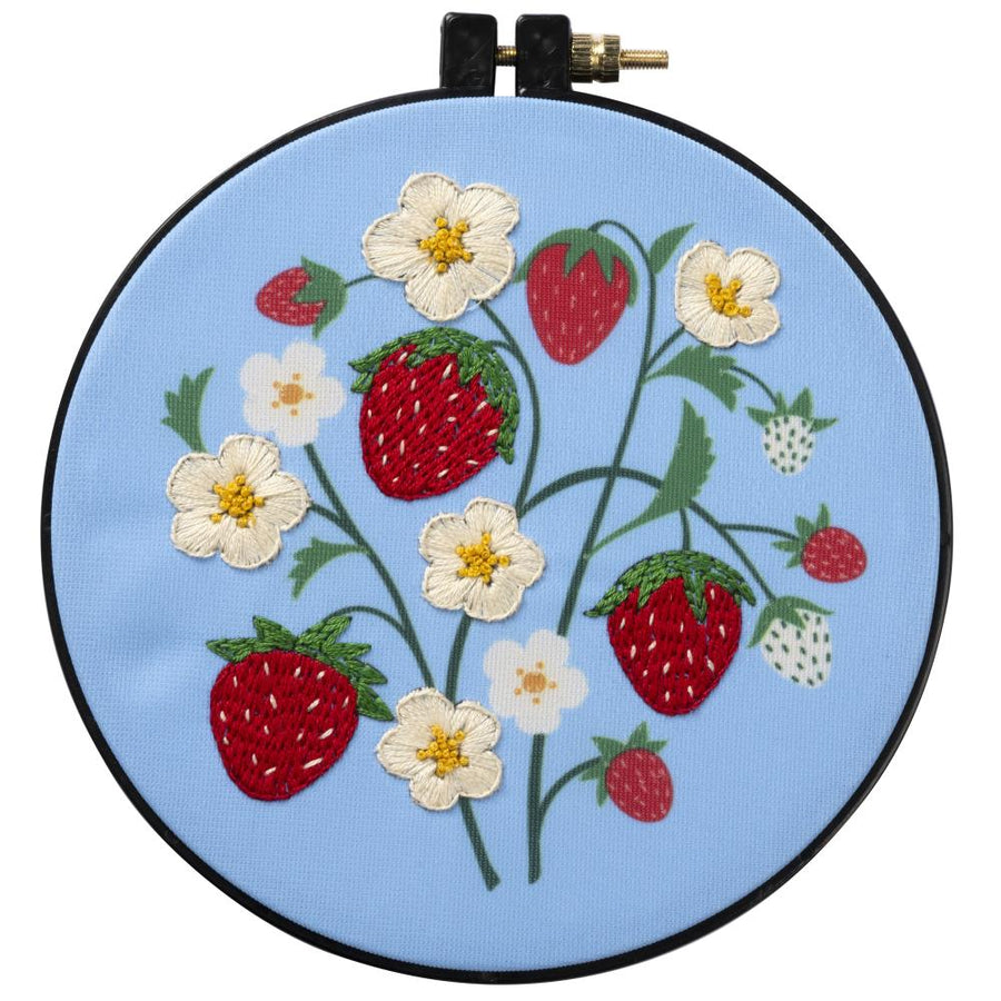 A beginner-friendly Bucilla stamped embroidery kit titled 'Strawberry Field.' The image shows a charming design of ripe red strawberries and delicate white blossoms. The kit features a 6-inch plastic hoop, colored printed polyester broadcloth, vibrant cotton embroidery floss, and a needle, perfect for a quick and rewarding 15cm round project
