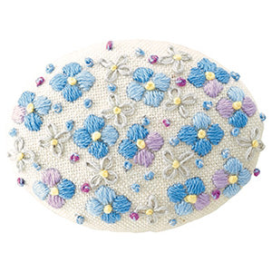 An embroidered brooch kit with a floral design, including pink and green threads on a pink fabric base, with a brooch pin and cotton thread visible.