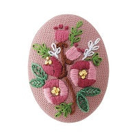 An embroidered brooch kit with a floral design, including pink and green threads on a pink fabric base, with a brooch pin and cotton thread visible.