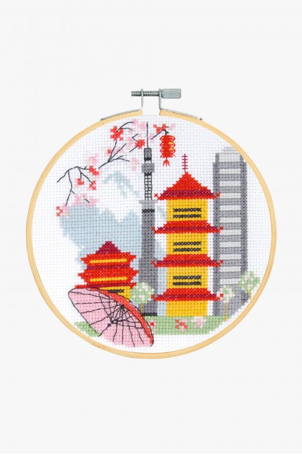 Cross stitch kit depicting a stylized cityscape with buildings and a traditional Japanese umbrella, completed in a 6-inch hoop.
