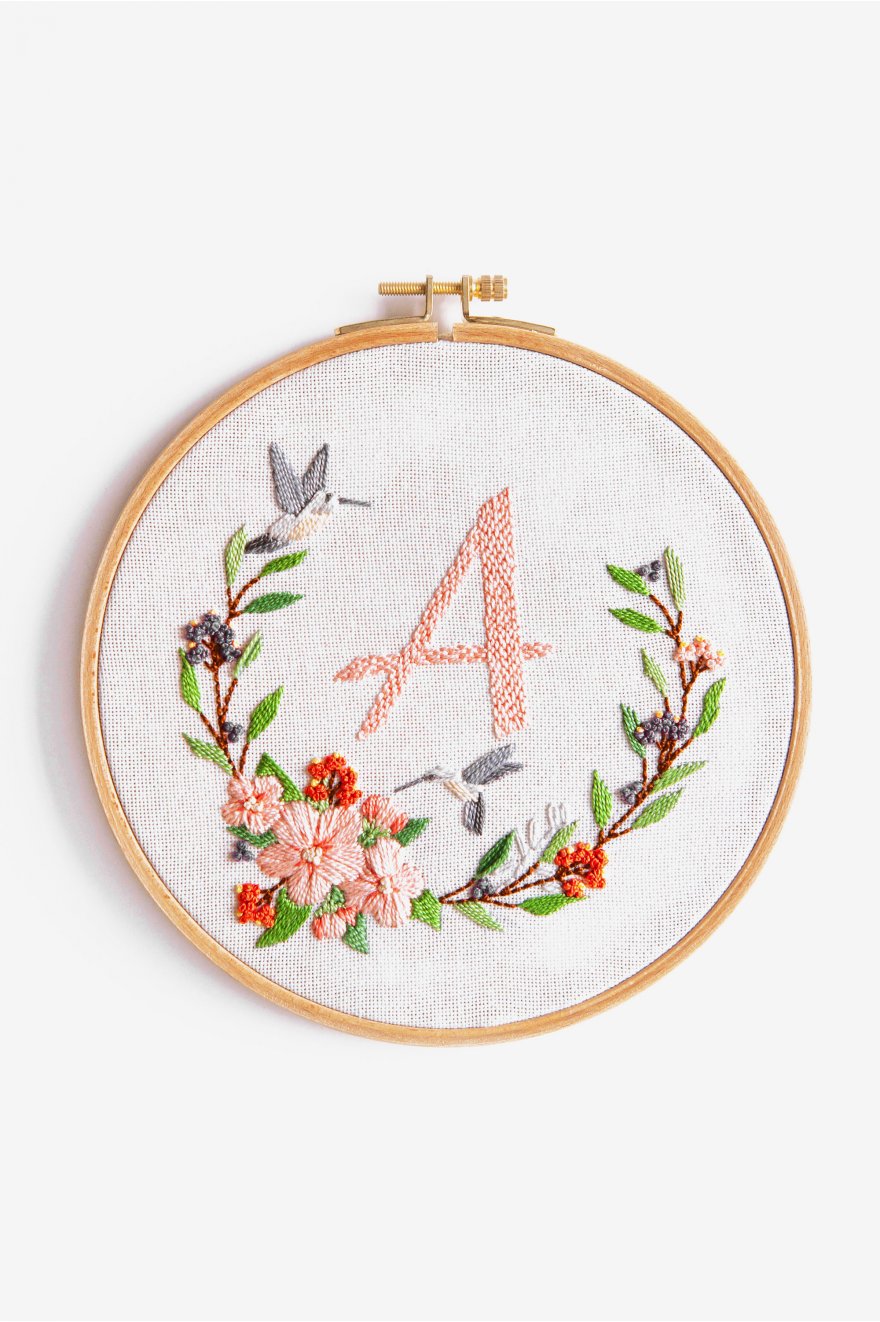 An advanced DMC 3D embroidery kit featuring a large, elegant circular garland of various flowers and leaves. The design is worked in thick Size 5 Pearl Cotton on 25-count evenweave fabric, creating a high-relief textured finish. The center is customizable with an included alphabet chart. The kit includes a large embroidery hoop, 50 strands of Pearl Cotton in 14 vibrant colors, and a needle for a 16-inch finished piece.