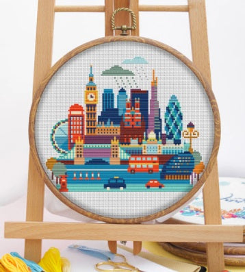 An elegant DMC counted cross-stitch kit from the Travel Series featuring the London cityscape. The design showcases iconic landmarks like Big Ben, the London Eye, and Tower Bridge in a refined color palette. The kit includes 14-count white Aida cloth, pre-sorted DMC embroidery floss, a needle, and easy-to-follow instructions.