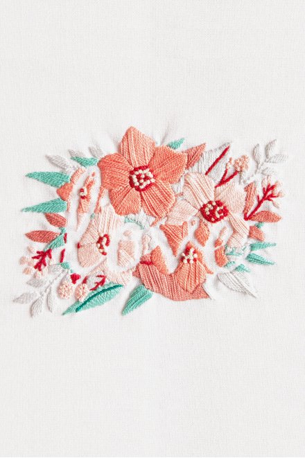 An intermediate DMC 3D embroidery kit featuring the word 'Love' beautifully entwined with vibrant, stylized flowers and swirling botanical vines. The design is worked in extra-thick Size 3 Pearl Cotton on a 25-count evenweave fabric with a pre-printed pattern. The kit includes 53.6 yards of thread in 8 romantic colors, a thread card, and a needle.