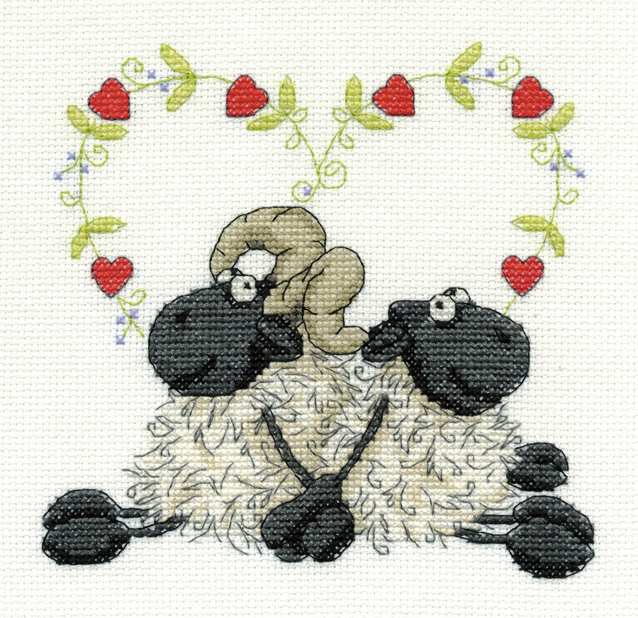 A charming DMC counted cross-stitch kit titled 'Love You Too.' The design features a stylized ram and ewe sitting back-to-back in a symmetrical pose, with a small red heart floating above them. The kit includes 14-count white Aida cloth, premium DMC embroidery floss, a tapestry needle, and clear instructions for a 6x6 inch finished piece.