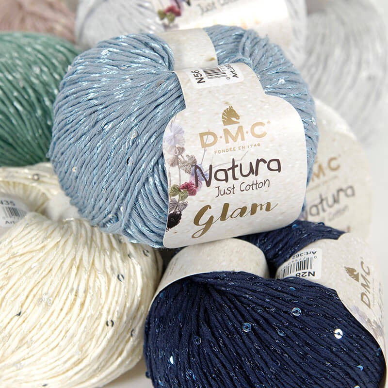 Several skeins of DMC Natura Glam yarn in various colors including blue, beige, and navy, with sequins added to the yarn.