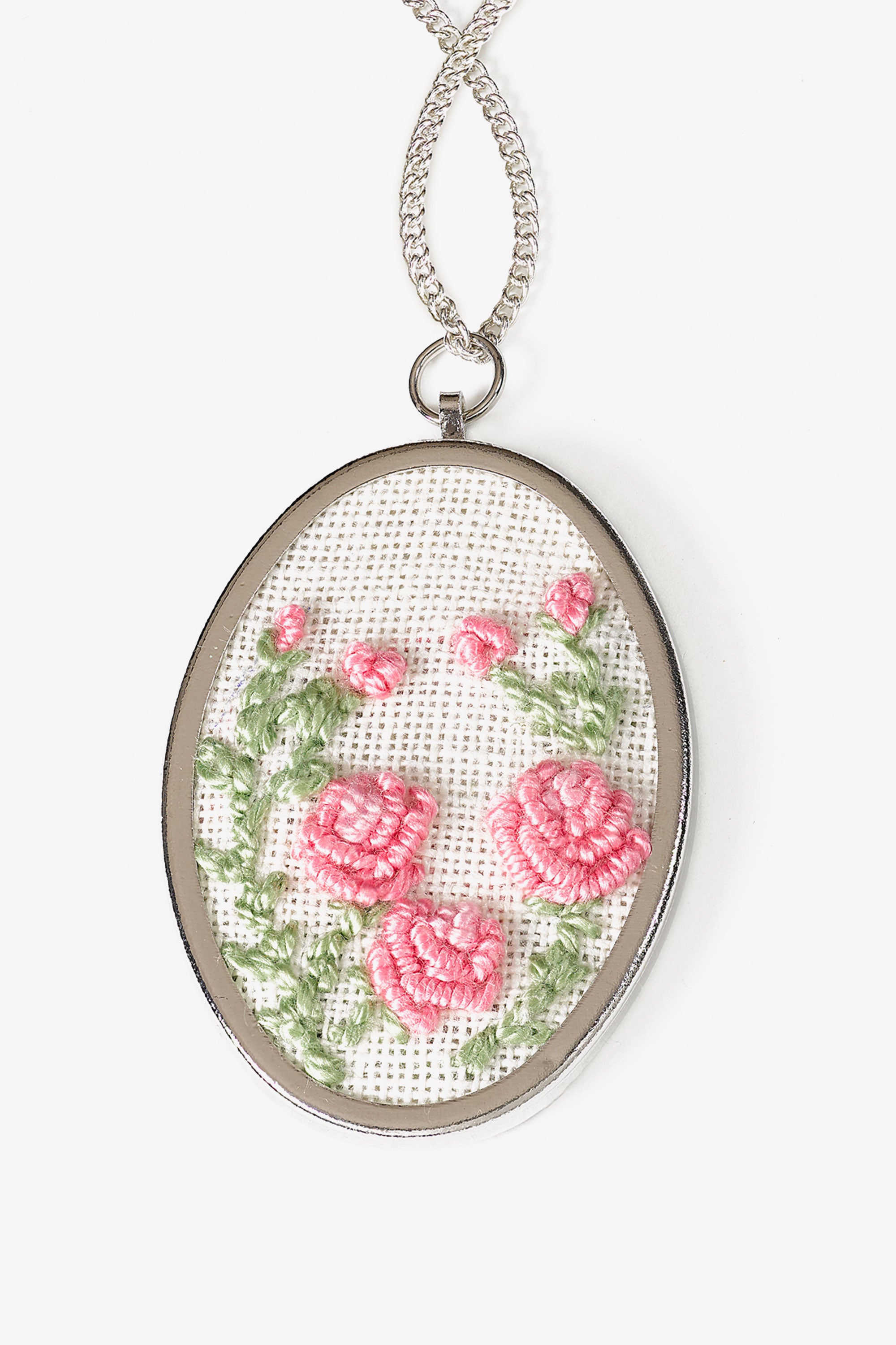 A professional-quality oval metal pendant frame by DMC, designed for custom embroidery inserts. The pendant features a classic polished finish and measures 5cm by 3.5cm. It comes complete with a matching delicate metal chain. This is a mounting base only, featuring a recessed area for securing a finished piece of needlework or cross-stitch fabric