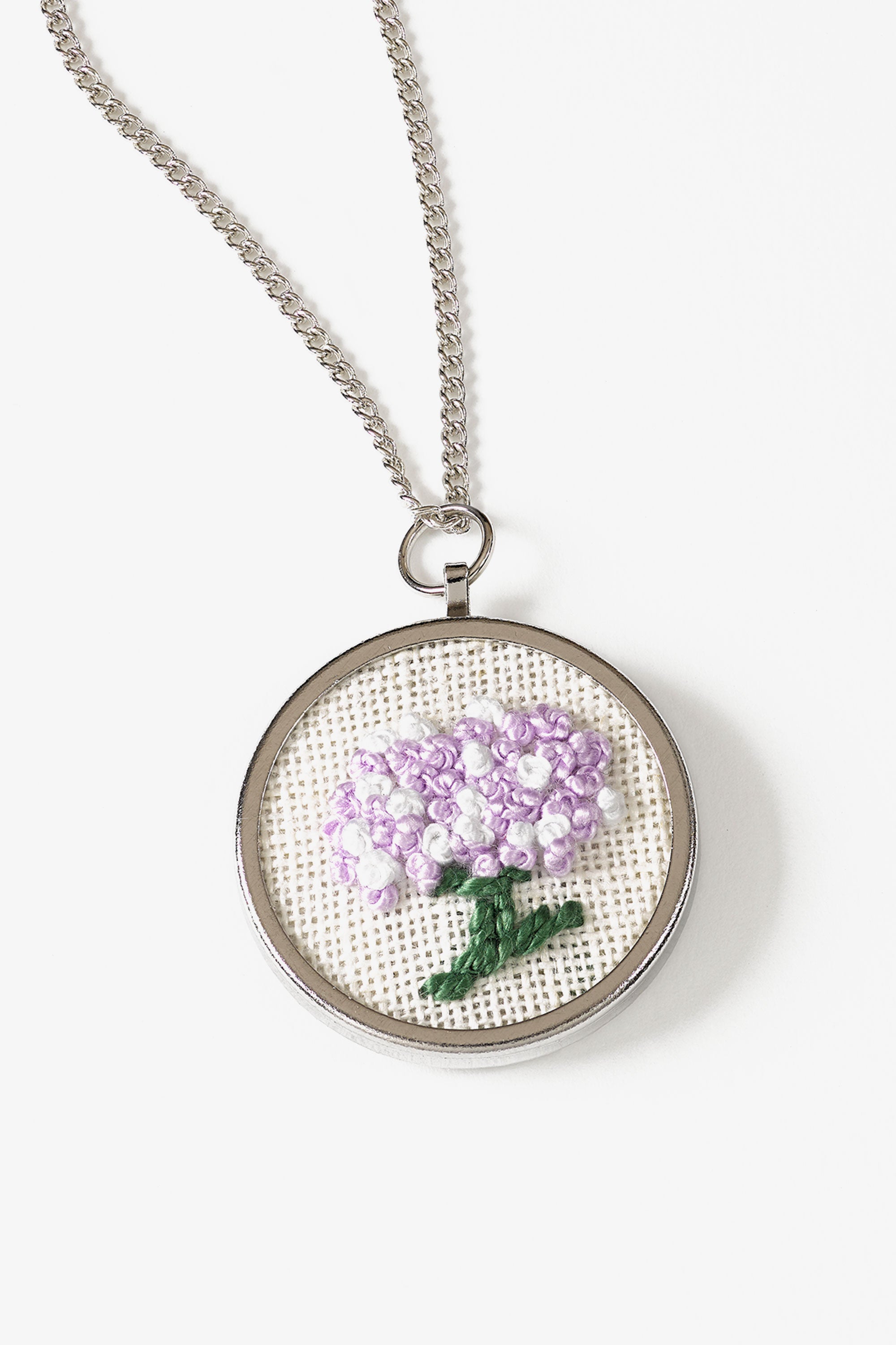 A high-quality circular metal pendant frame by DMC, specifically designed for mounting custom embroidery or cross-stitch inserts. The pendant has a 3cm diameter and a polished, professional finish. It comes with a matching delicate metal chain. This is a mounting base only, featuring a recessed center for securing your finished fabric art