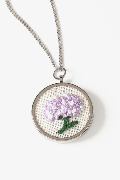 A high-quality circular metal pendant frame by DMC, specifically designed for mounting custom embroidery or cross-stitch inserts. The pendant has a 3cm diameter and a polished, professional finish. It comes with a matching delicate metal chain. This is a mounting base only, featuring a recessed center for securing your finished fabric art