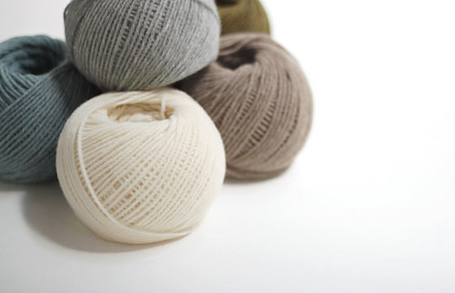 Several skeins of Daruma Airy Wool Alpaca yarn in various shades of beige, brown, and gray.