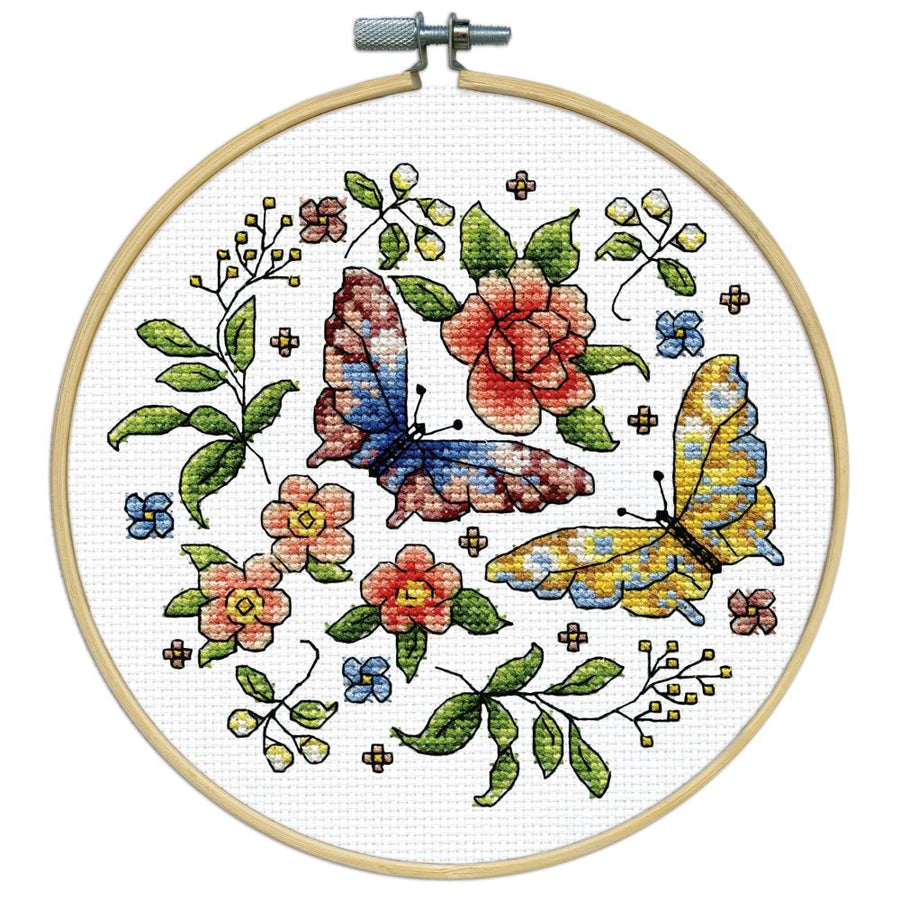 A beginner-friendly Design Works counted cross-stitch kit featuring a 'Butterflies' and floral design. The kit includes 11-count white Aida fabric, a pre-sorted 100% cotton thread palette, a needle, and an 8-inch circular hoop. The packaging highlights the vibrant, cheerful colors and the all-in-one convenience of the set