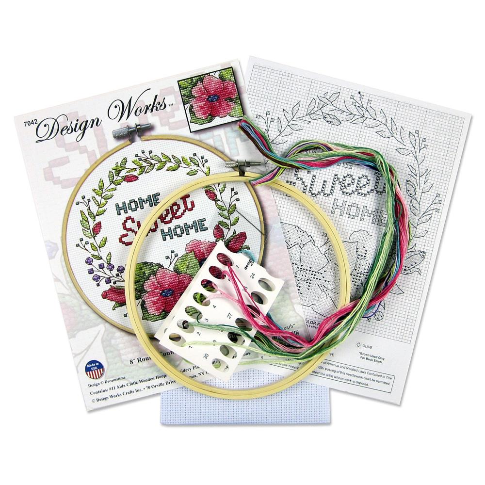 A beginner-friendly Design Works counted cross-stitch kit featuring a 'Floral Wreath' design. The image showcases a classic circular garland of pink flowers with green leaves. The kit includes 11-count white Aida fabric, a pre-sorted 100% cotton thread palette, a needle, and an 8-inch circular hoop for stitching and display