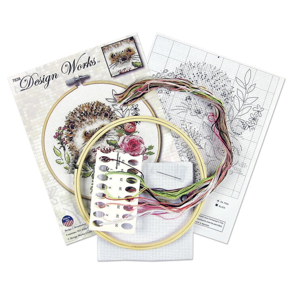 A beginner-friendly Design Works counted cross-stitch kit featuring a cute hedgehog design. The kit includes 11-count white Aida fabric, a pre-sorted 100% cotton thread palette, a tapestry needle, and an 8-inch circular hoop. The packaging highlights the whimsical, kid-friendly illustration and the all-in-one convenience of the set