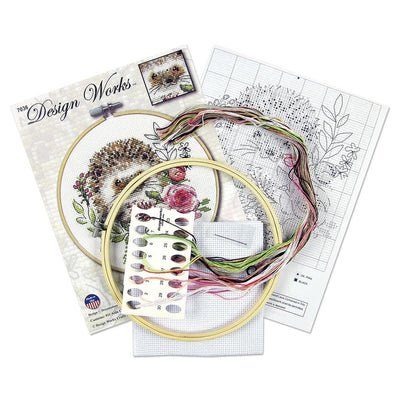 A beginner-friendly Design Works counted cross-stitch kit featuring a cute hedgehog design. The kit includes 11-count white Aida fabric, a pre-sorted 100% cotton thread palette, a tapestry needle, and an 8-inch circular hoop. The packaging highlights the whimsical, kid-friendly illustration and the all-in-one convenience of the set