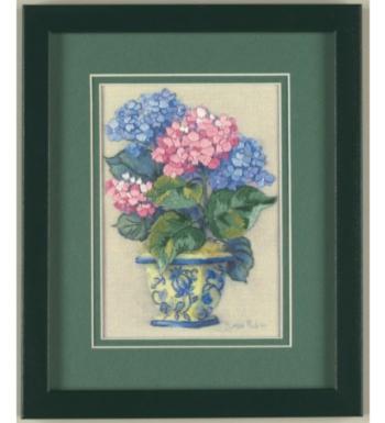 A framed crewel embroidery kit depicting colorful hydrangeas in a blue and white vase, with a green border.