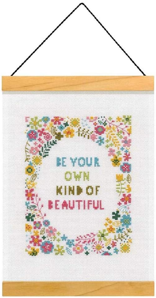 An elegant Dimensions counted cross-stitch kit featuring a large bouquet of detailed flowers in pinks, purples, and greens surrounding the inspirational quote 'Be Your Own Kind of Beautiful.' The kit includes 14-count white Aida, embroidery thread, a needle, and two wooden strips for a decorative hanging finish