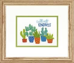 A colorful Dimensions embroidery kit featuring five decorative pots of varying sizes and patterns. Inside the pots are several varieties of cacti and vibrant desert wildflowers. The phrase 'cultivate kindness' is written in a graceful blue script above the plants. The kit includes pre-printed fabric, embroidery floss, and a needle for a 7x5 inch finished piece