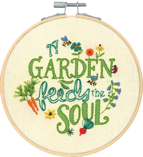 A charming Dimensions embroidery kit featuring a vintage-style watering can filled with a colorful variety of flowers like daisies and lavender. The phrase 'A Garden Feeds The Soul' is written in an elegant, flowing script. The design is pre-printed on fabric and includes a 6-inch embroidery hoop, colorful threads, and a needle.