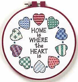 A cross-stitch depiction of the phrase 'Home is where the heart is' with various colored hearts and a plastic hoop.