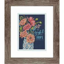 An elegant Dimensions counted cross-stitch kit titled 'Joyful Floral.' The design features soft, pastel-colored flowers and greenery surrounding the gold and white script 'Be Joyful in Hope.' The entire scene is set against a deep Navy 14-count Aida cloth, creating a high-contrast, luminous effect. The kit includes fabric, all necessary threads, a needle, and a pattern sheet for a 5x7 inch finished piece