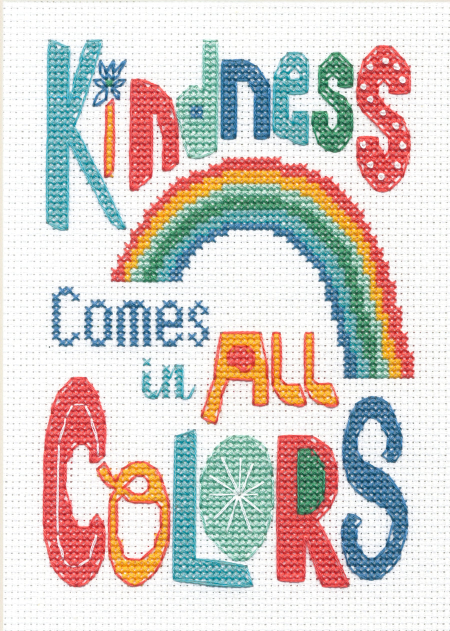 A bright and cheerful Dimensions counted cross-stitch kit titled 'Kindness Colors.' The design features the phrase 'Kindness colors the world' in a mix of playful fonts, accented by a rainbow of floral or geometric motifs. The kit includes 14-count white Aida fabric, all necessary embroidery threads, a needle, and a clear pattern sheet for a 5x7 inch finished piece