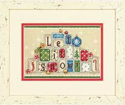 A festive Dimensions counted cross-stitch kit titled 'Let It Snow.' The design features colorful toy building blocks stacked in a pyramid shape to spell out the holiday phrase. Accented with winter motifs, the kit includes 14-count white Aida cloth, cotton embroidery thread, a needle, and easy-to-follow instructions for a 7x5 inch finished piece