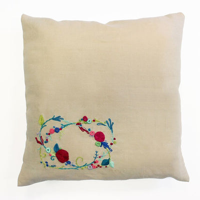 A cushion cover with a floral embroidery design in the center, featuring a rose garland motif.
DMC Sweet Meadow Rose Garland embroidery kit packaging, showing a stunning finished floral wreath cushion on a rustic chair.