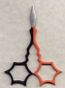 A pair of embroidery scissors with a lightening bolt design, featuring spider web shaped finger holes; painted half orange and half black.