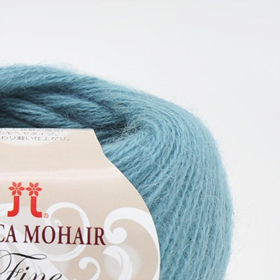 A 25g ball of Hamanaka Alpaca Mohair Fine yarn, showcasing its soft, fuzzy halo and fine, delicate strand. The image highlights the airy texture created by the blend of goat mohair and high-grade alpaca, perfect for knitting or crocheting lightweight, fluffy wearables like scarves, vests, and cardigans in turquoise blue colour