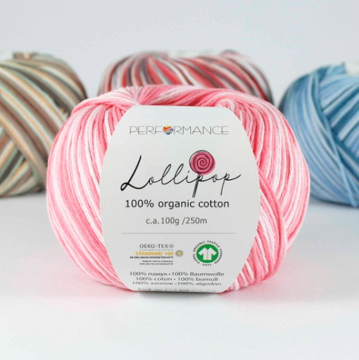 A skein of pink Lollipop brand organic cotton yarn with a label showing the brand name and yarn type, surrounded by other skeins of yarn in the background.