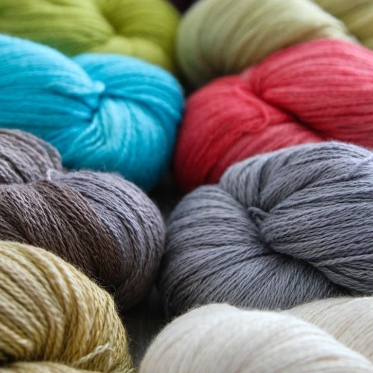 Bundles of hand-dyed silk/cashmere yarn in various colors including red, blue, gray, and green.
