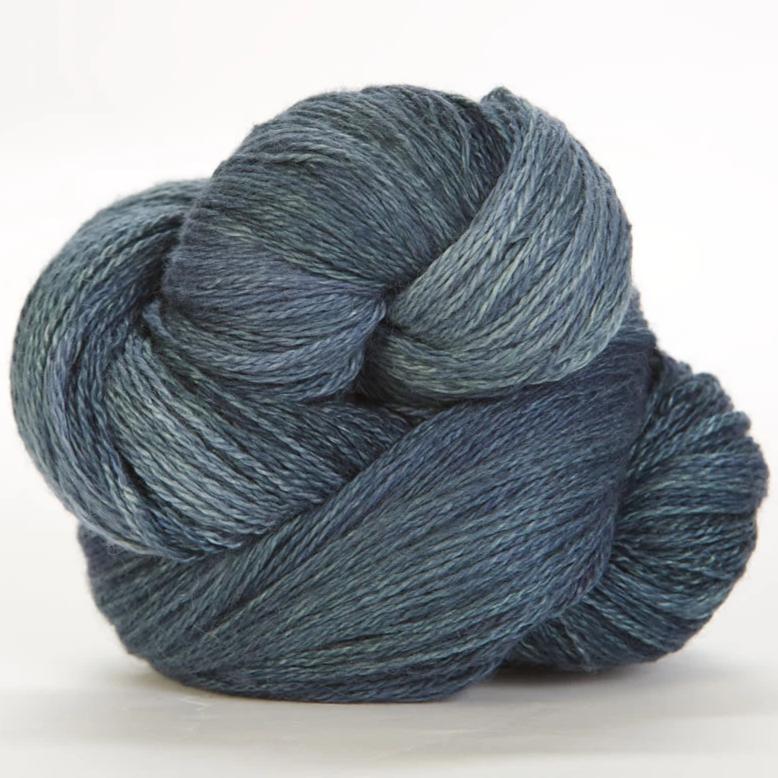 Jade Sapphire hand-dyed 50% silk and 50% yak lace yarn from Mongolia; a 100g skein with 700 yards for premium lace knitting."
"Close-up of hand-dyed Jade Sapphire exotic fiber yarn in dark blue jeans, showing the unique tonal variations and silken luster of the yak-silk blend."
