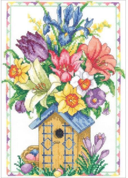 A vertical-format cross-stitch kit from Janlynn titled 'Spring Birdhouse.' The design features a beautifully detailed wooden birdhouse draped in lush spring blossoms, with a colorful songbird perched nearby. The style is classic and painterly, utilizing a soft palette of petal pinks, sky blues, and garden greens. The kit includes 14-count white cotton Aida, carded six-strand cotton floss, and a needle. The finished design measures 9 by 12 inche