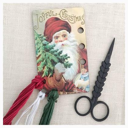 A wooden thread holder with a vintage Christmas postcard design featuring Santa Claus and a Christmas tree. The product is approximately 9.