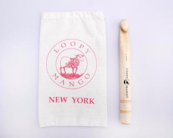 A large crochet hook lying on a textured surface, next to a white drawstring bag with the Loopy Mango brand logo.

A 25mm Loopy Mango giant wooden crochet hook, showcasing its impressive diameter and smooth, natural wood grain with professional branding