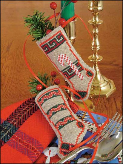 A finished pair of cross-stitched linen candy cane stockings, featuring delicate greenery and berry sprigs, displayed as elegant Christmas tree ornaments