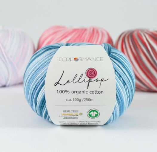 A skein of blue Lollipop brand organic cotton yarn with a label showing the brand name and yarn type, surrounded by other skeins of yarn in the background.