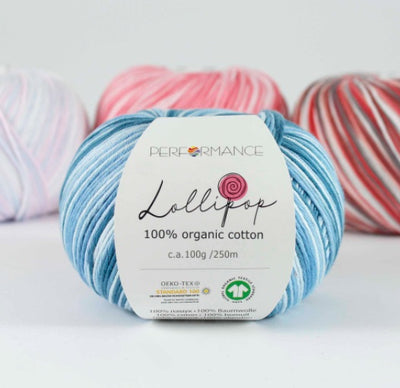 A skein of blue Lollipop brand organic cotton yarn with a label showing the brand name and yarn type, surrounded by other skeins of yarn in the background.