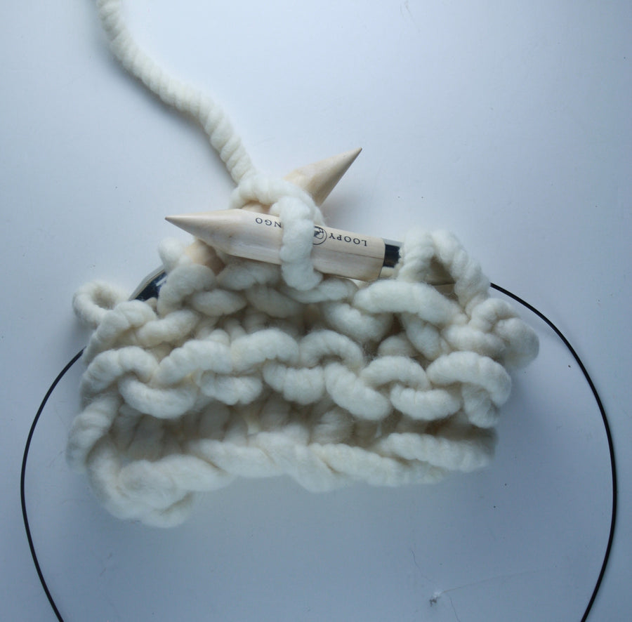 A pair of giant circular knitting needles made from birch wood, with a flexible plastic connecting wire, resting on a knitted fabric.

25mm giant circular needles coiled next to a ball of chunky yarn, demonstrating their compact, travel-friendly size