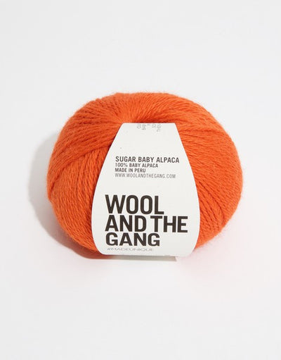 A blue skein of WOOL AND THE GANG Sugar Baby Alpaca yarn with a label in the center in rusty orange colour