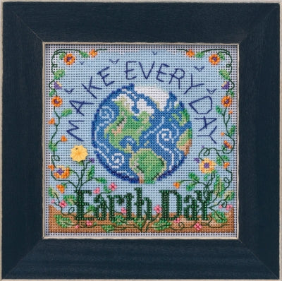 A framed cross stitch kit depicting a colorful Earth Day message with floral and planetary designs.